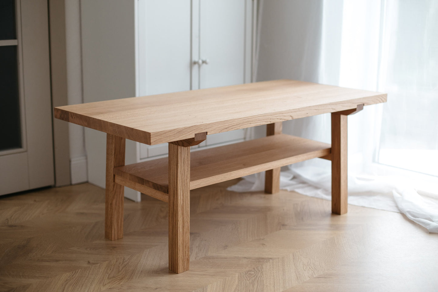 A handmade wooden coffee table made of natural oak, featuring a simplistic and Scandinavian design with a lower shelf.
