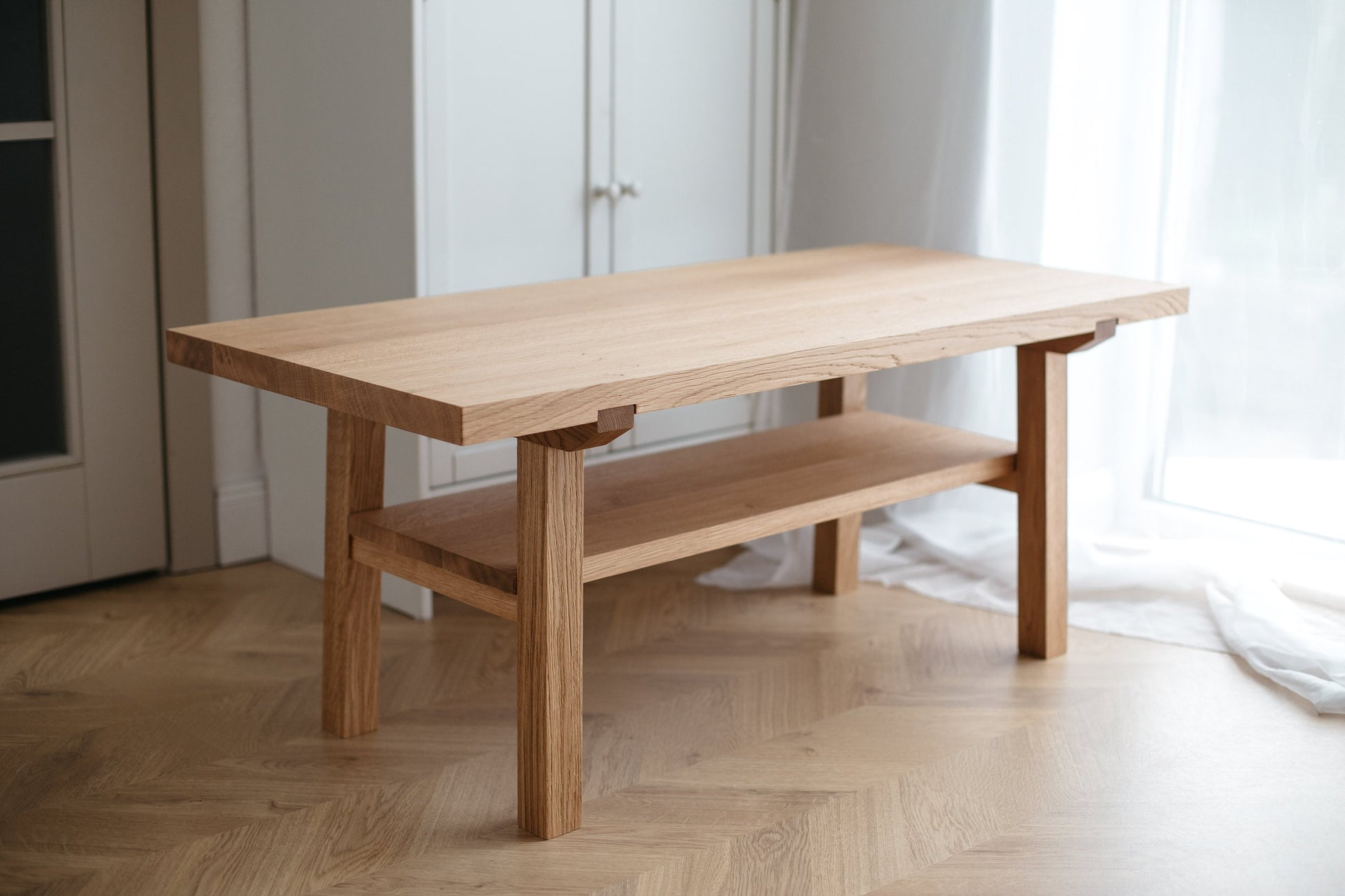 A handmade wooden coffee table made of natural oak, featuring a simplistic and Scandinavian design with a lower shelf.
