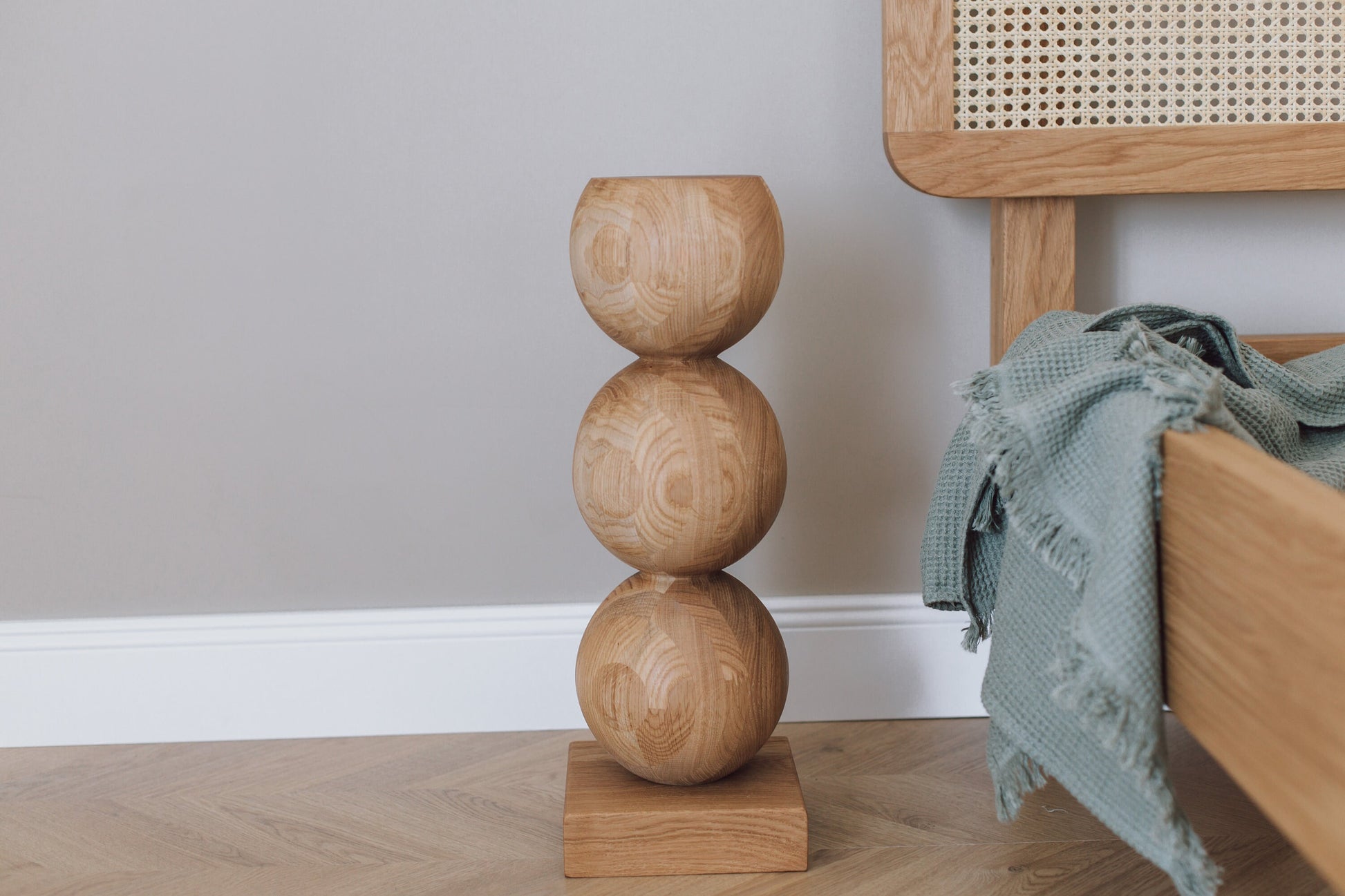 A handcrafted wooden bedside table with a central sphere accent, placed on a light-colored floor next to a bed with a blue blanket.