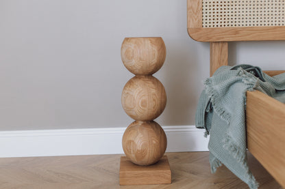 A handcrafted wooden bedside table with a central sphere accent, placed on a light-colored floor next to a bed with a blue blanket.