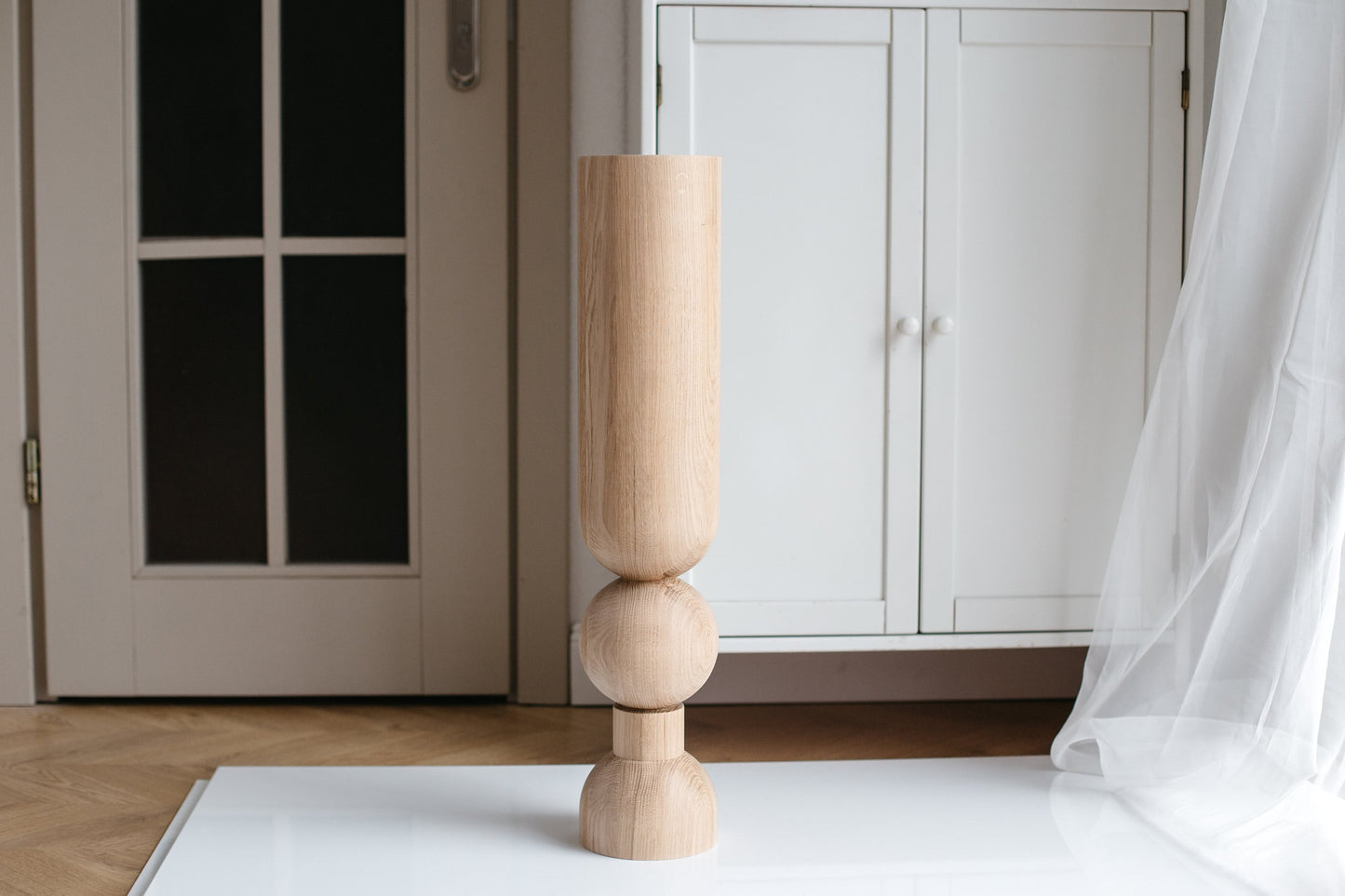 A single beige wooden furniture leg with a sphere on the bottom, standing upright on a flat surface.
