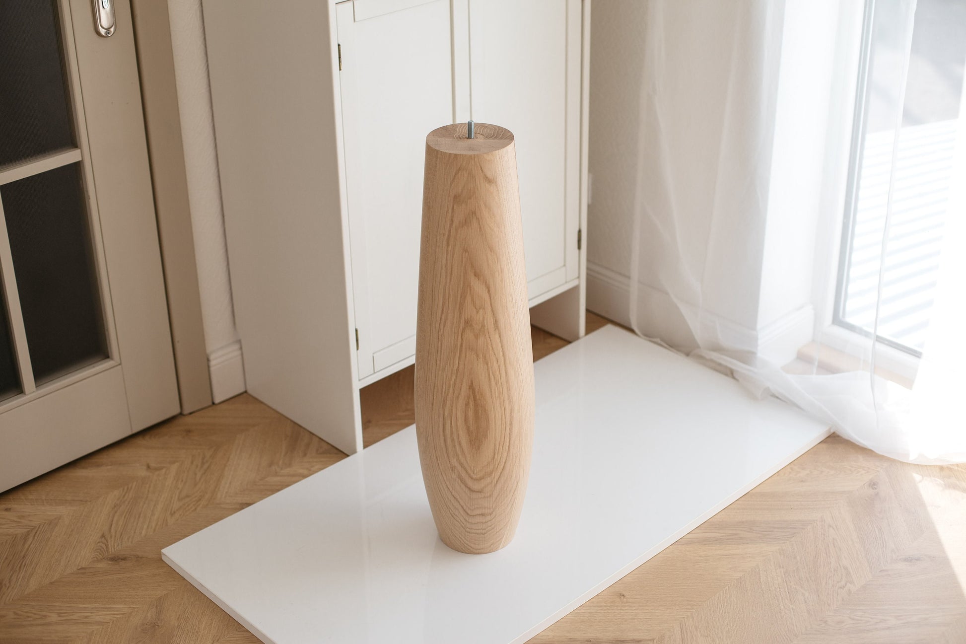 An oval wooden furniture leg, presumably a table leg, displayed against a white background with a light-colored floor.