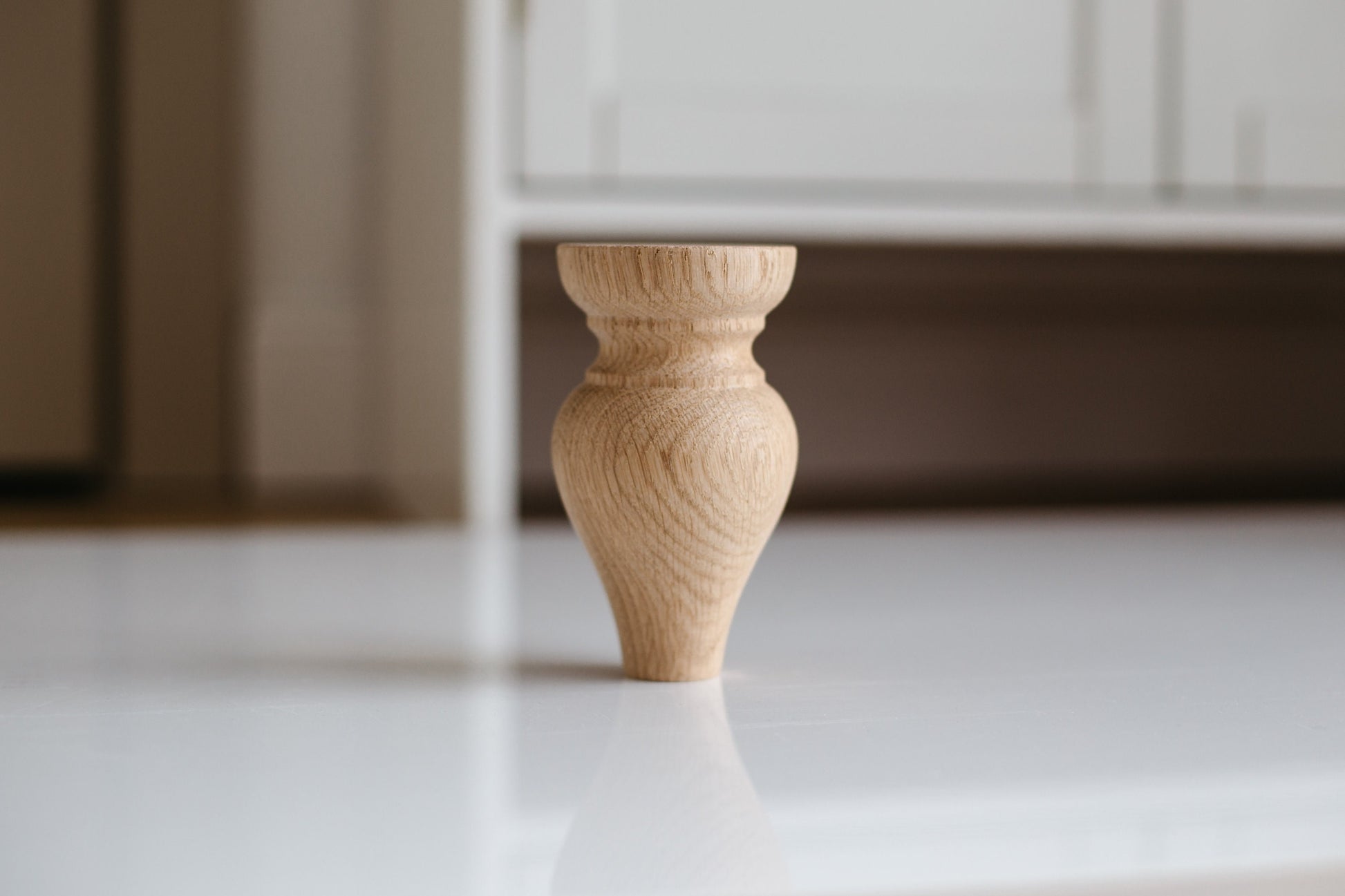 A single wooden furniture leg on a white floor, with a blurred background suggesting a home interior setting.