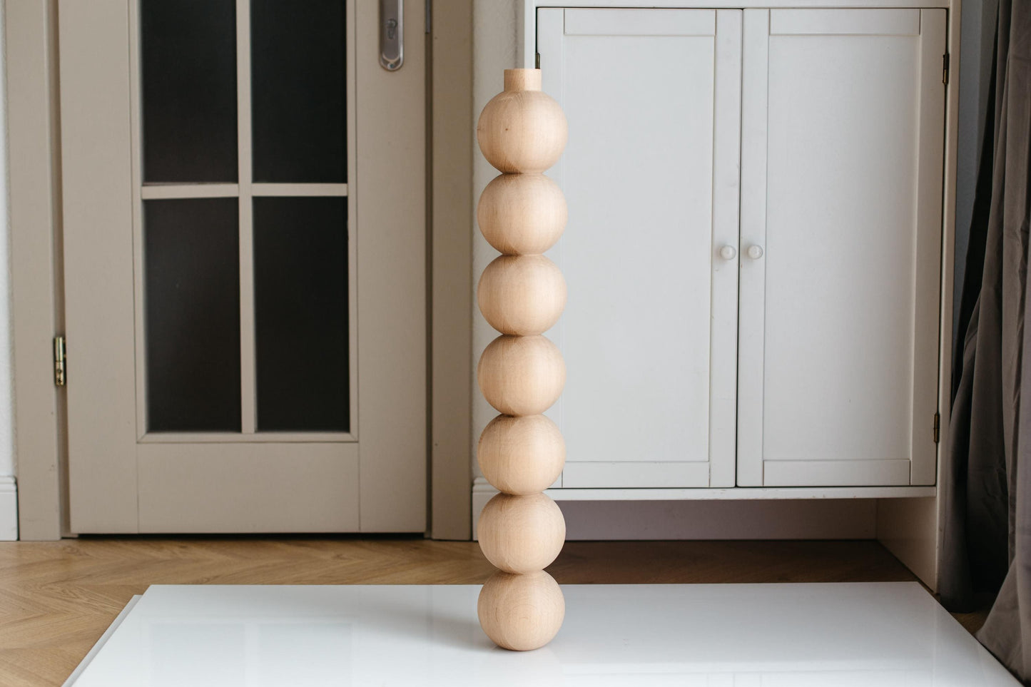 A handmade wooden furniture leg with seven spherical protrusions, displayed against an interior background.