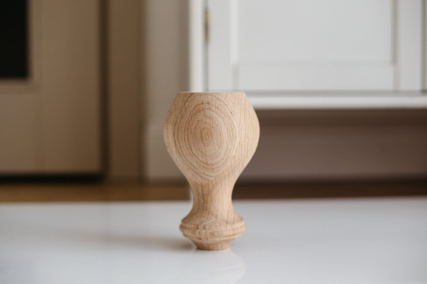 A single handmade wooden furniture leg with a sphere design, placed on a flat surface with a window in the background.