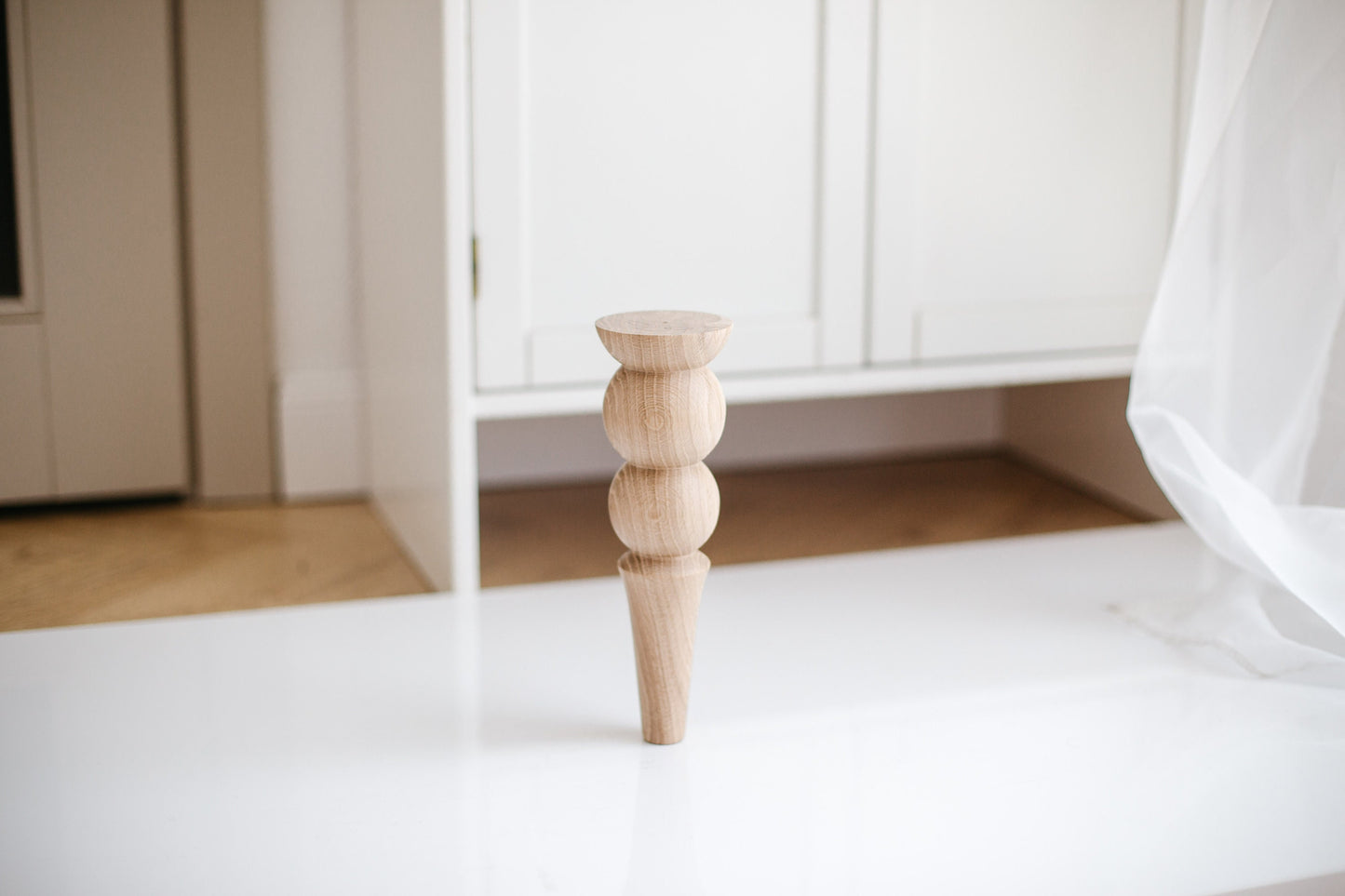 A single wooden furniture leg with a two balls design placed on a white surface with a piece of furniture visible in the background.
