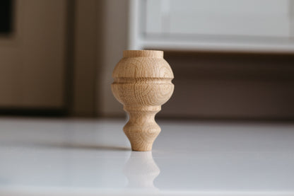 A single wooden furniture leg with a rounded shape at the top, placed on a flat surface.