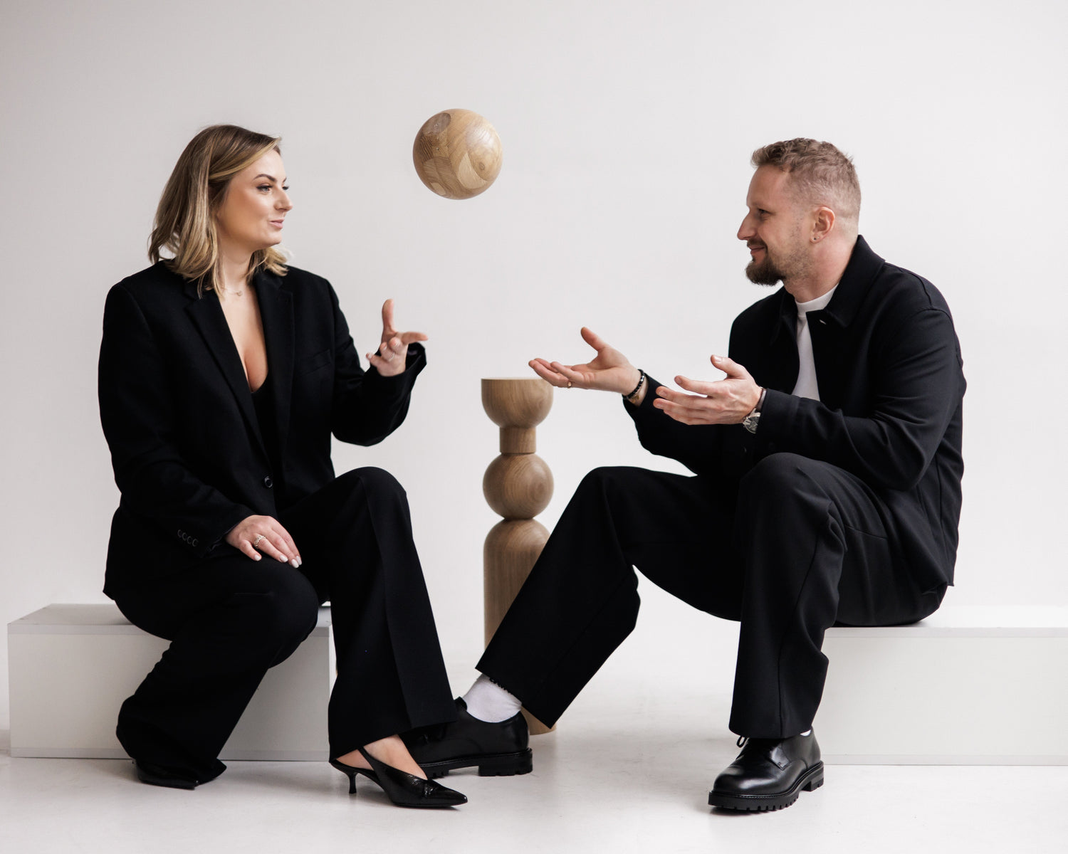 Two people in formal attire sitting on a white floor with a neutral background