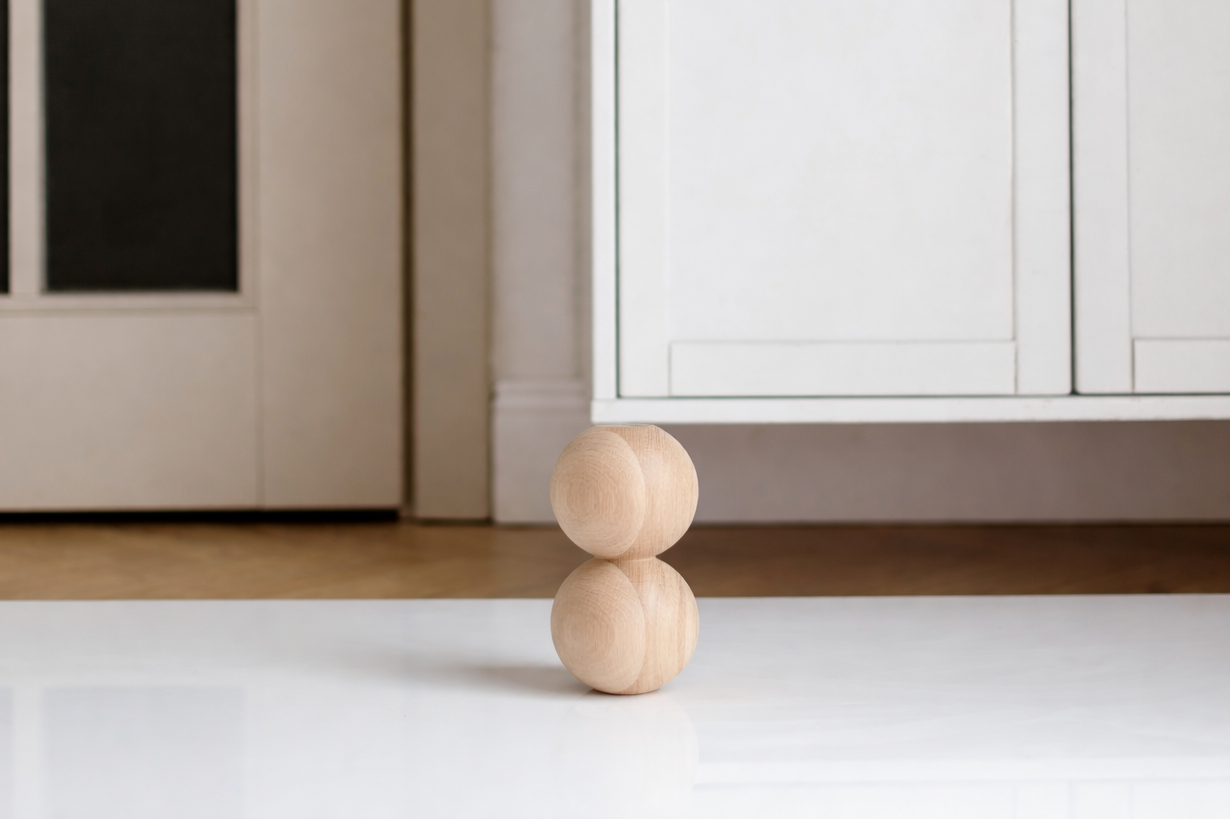 Two wooden spheres stacked on a white surface with a neutral-colored cabinet in the background.