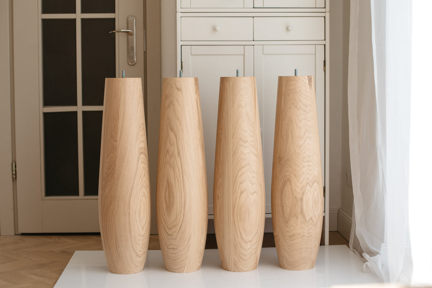 Four wooden vases of varying heights on a white surface with a neutral background.