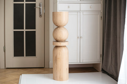 A single wooden furniture leg with a spherical design at the top, placed on a white surface, with a door and a white cabinet in the background.
