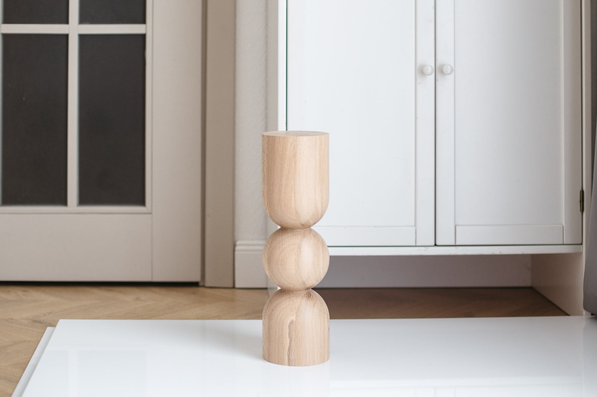 A single natural wooden coffee table leg with a sphere design on a flat surface, with a door and light fixture in the background.