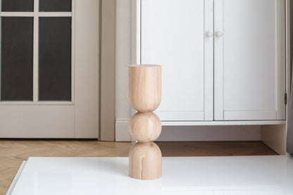A single natural wooden coffee table leg with a sphere design on a flat surface, with a door and light fixture in the background.