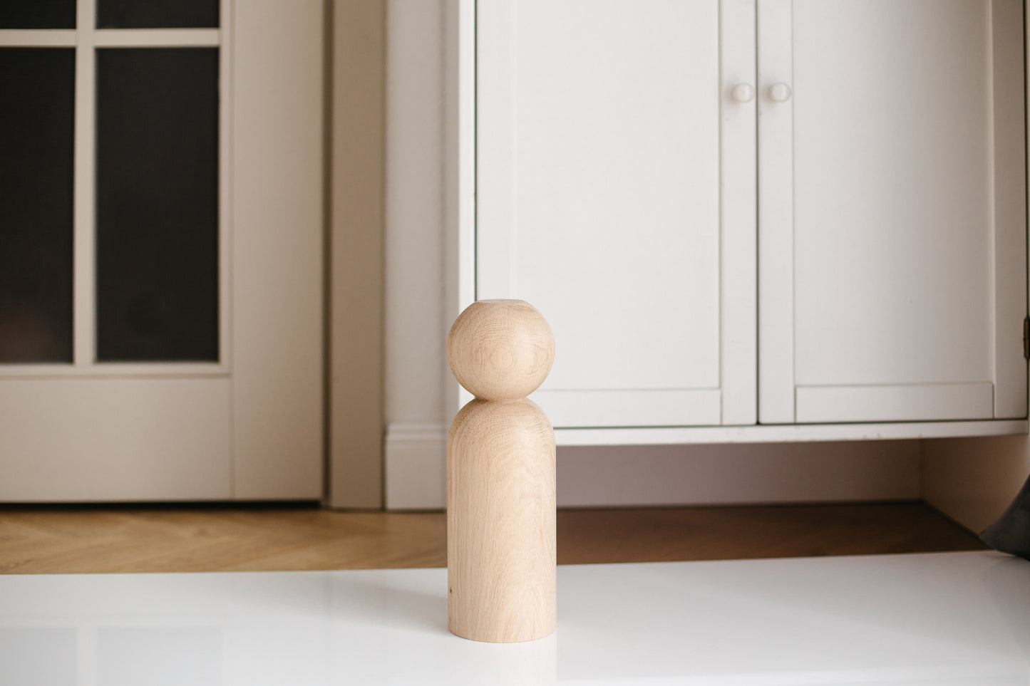Wooden peg figure on a white floor with cabinets in the background