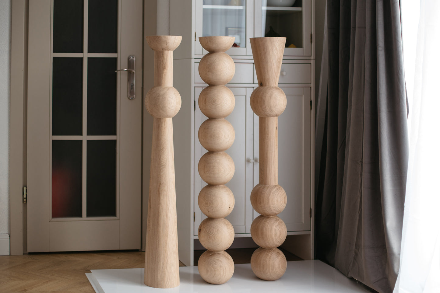 Three wooden candle holders of different designs on a white rug in a room.