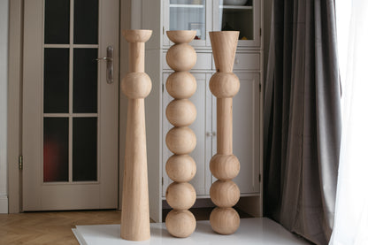 Three wooden candle holders of different designs on a white rug in a room.