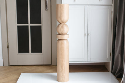 Wooden leg of a piece of furniture against a white cabinet and door.