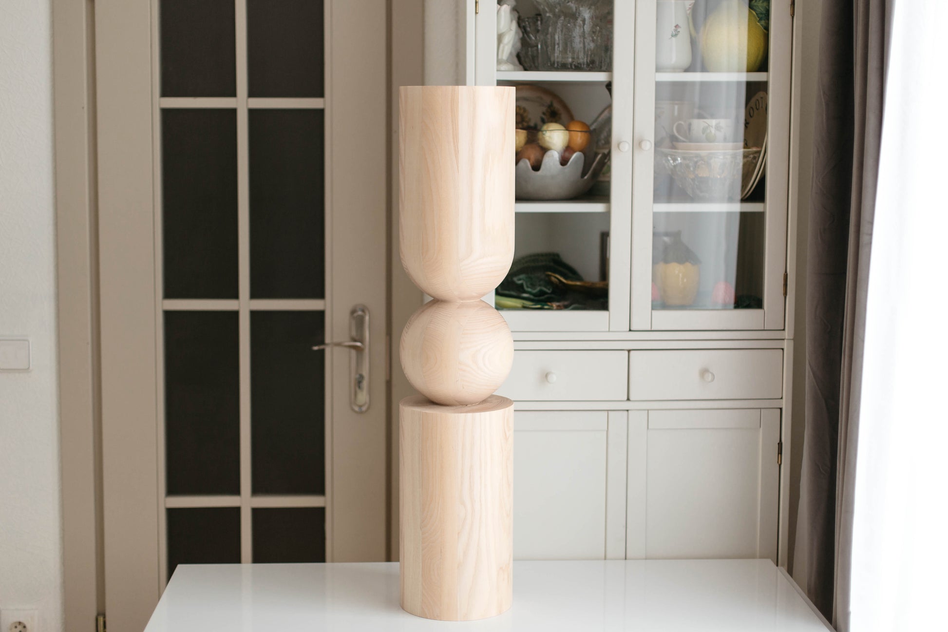 Decorative wooden sculpture on a white surface with a glass cabinet in the background.