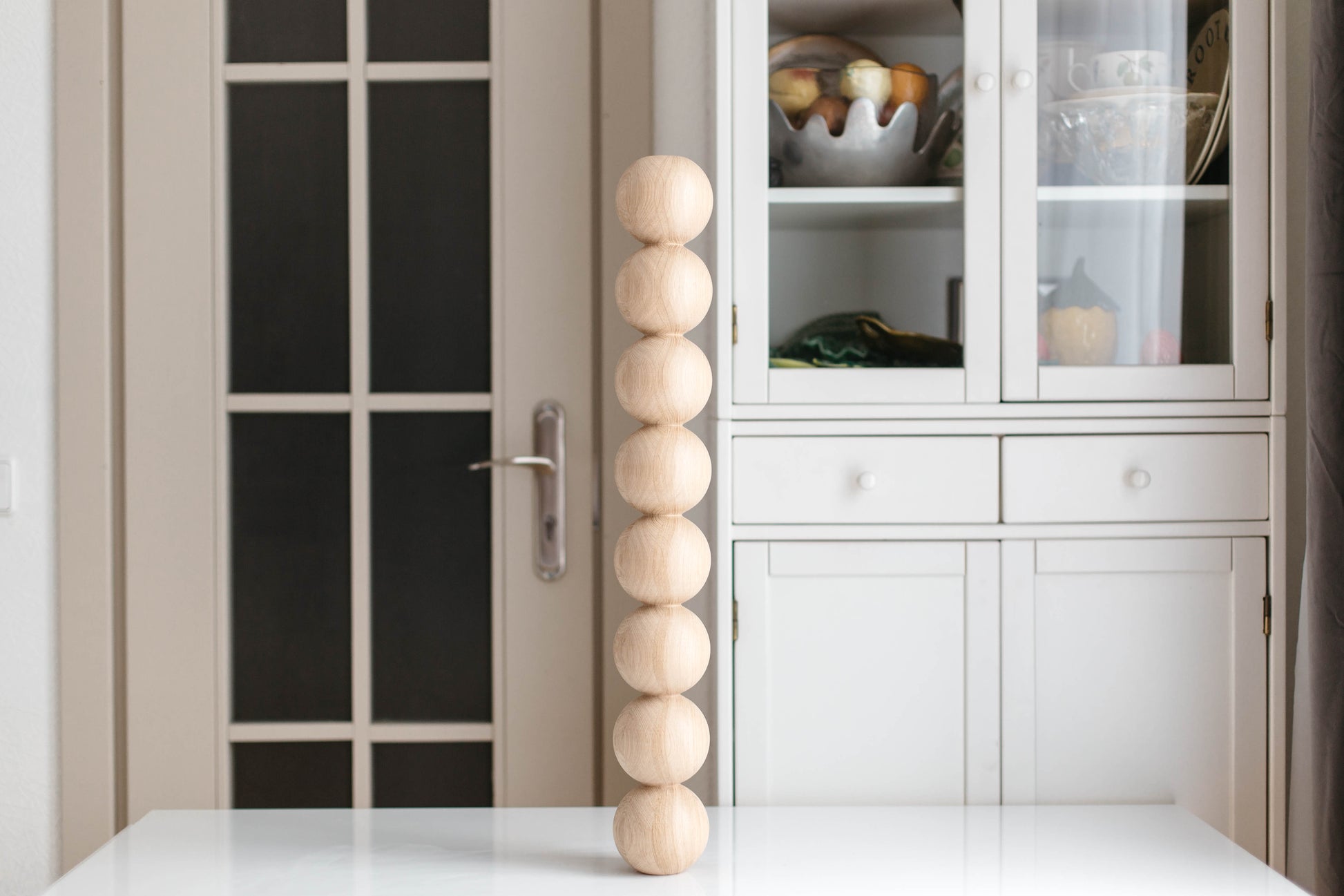 Decorative wooden sphere sculpture on a white surface with a glass cabinet in the background.