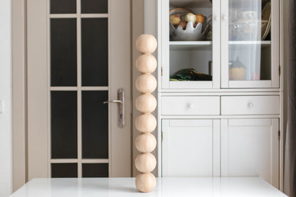 Decorative wooden sphere sculpture on a white surface with a glass cabinet in the background.