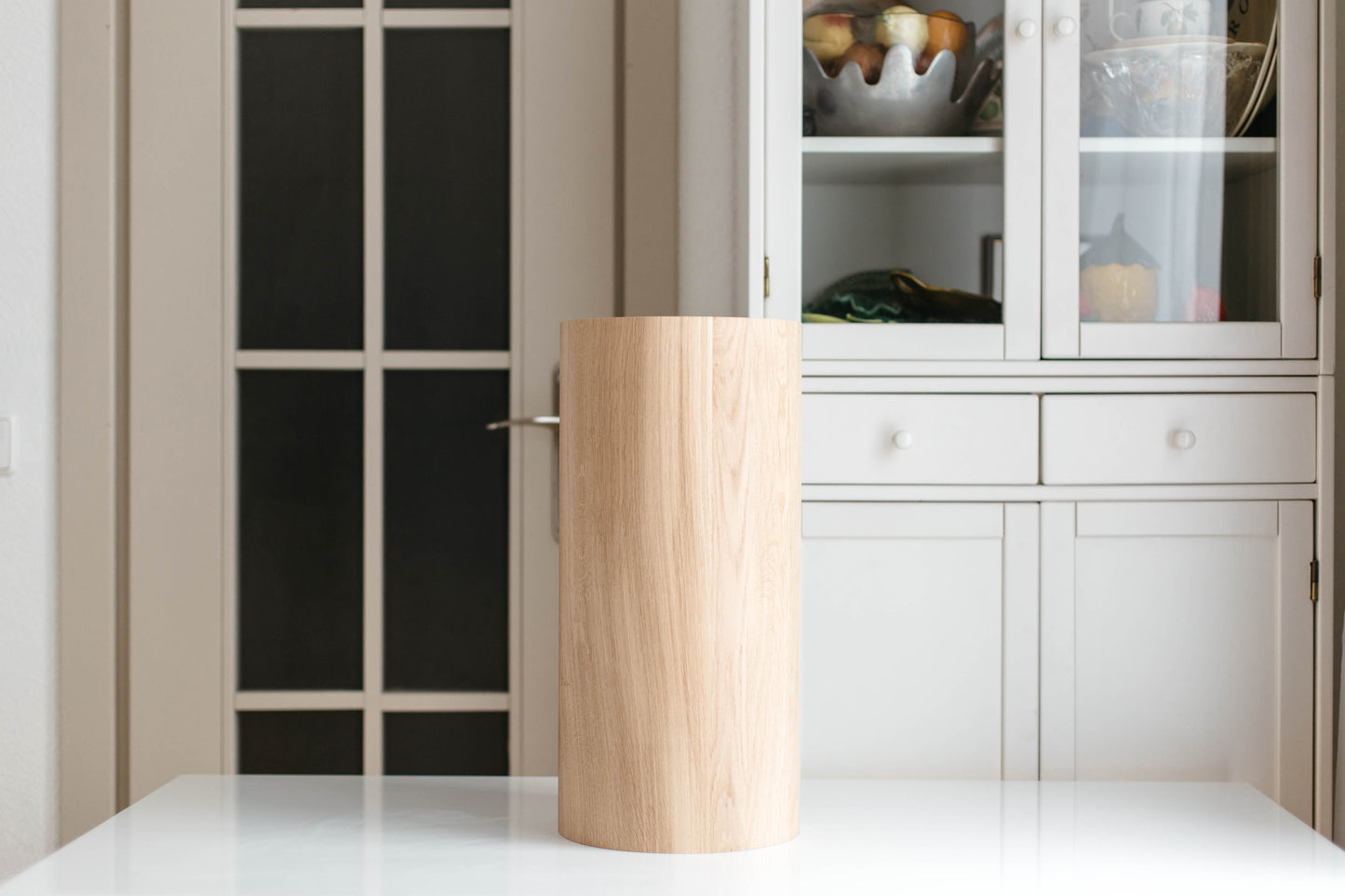 Wooden trash can on a white surface with a cabinet in the background