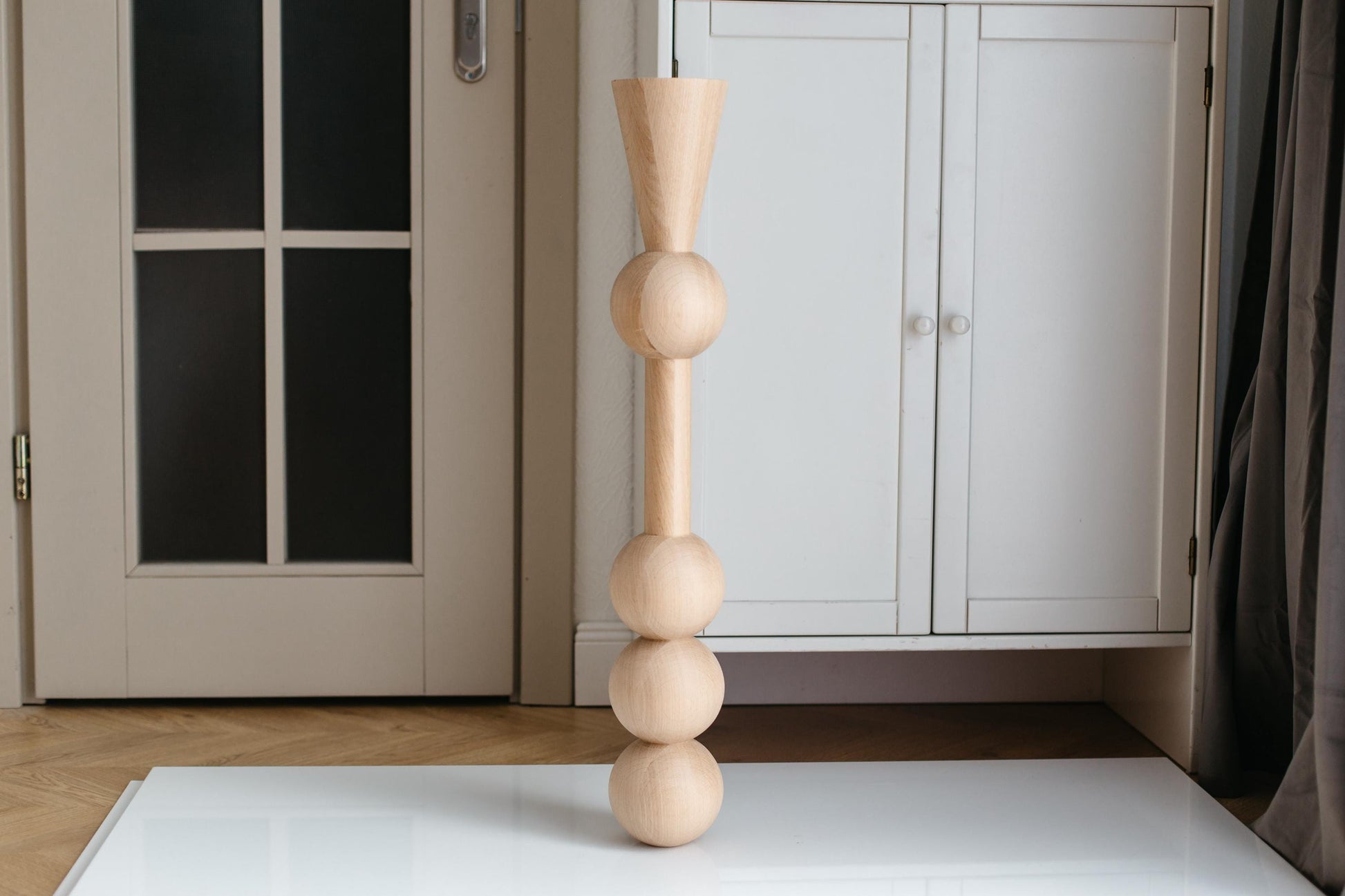 A handmade wooden furniture leg with three spheres, crafted from unfinished raw wood, displayed in an indoor setting.