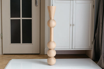 A handmade wooden furniture leg with three spheres, crafted from unfinished raw wood, displayed in an indoor setting.