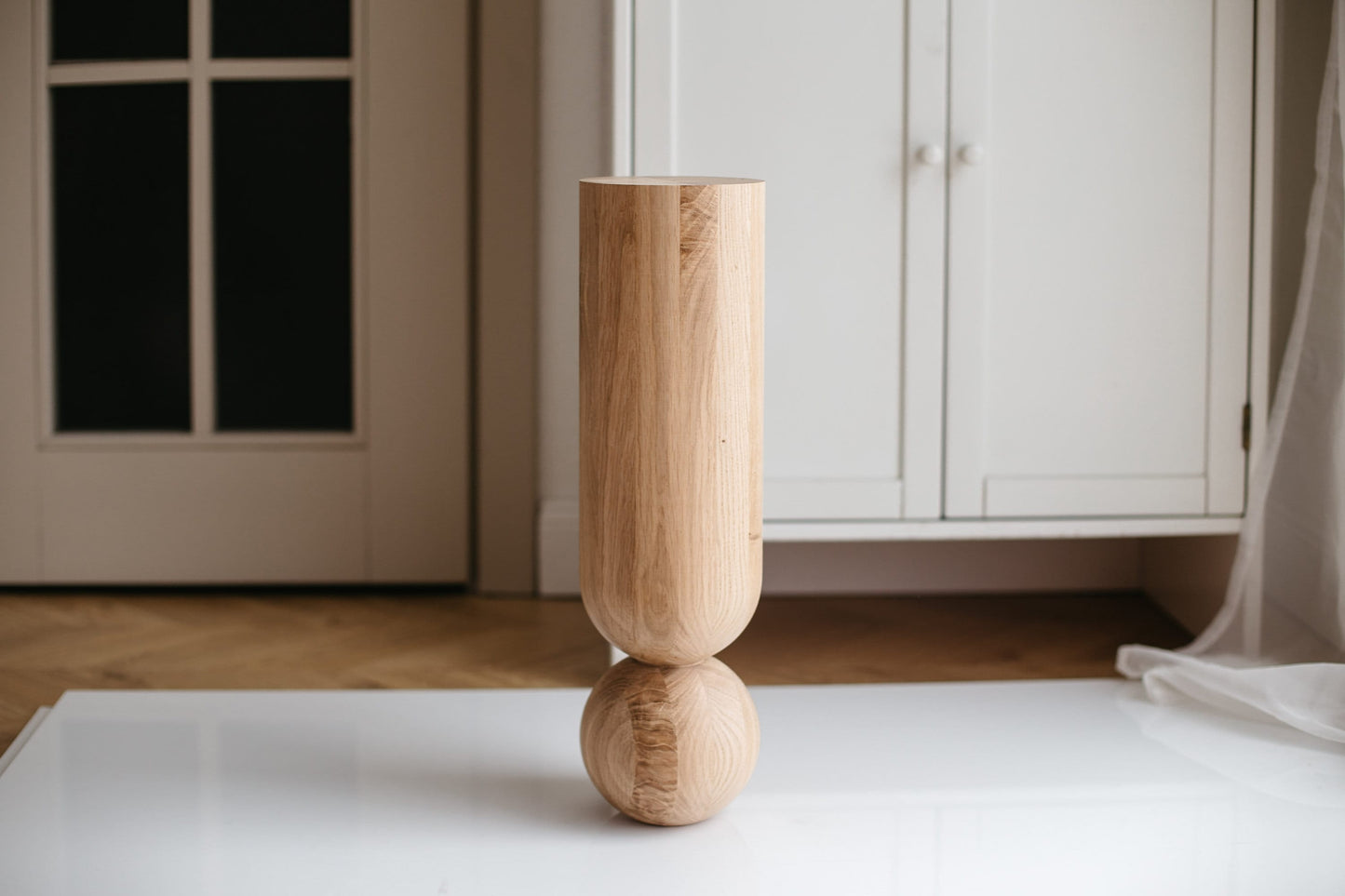 A single natural wooden coffee table leg with a sphere, displayed against an indoor background.