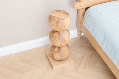Wooden spherical object on a wooden stand against a neutral wall with a bed in the background.